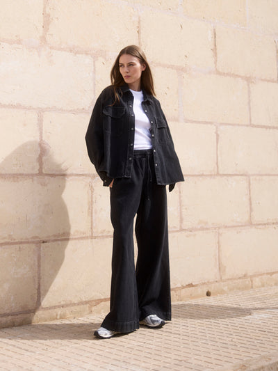 Damen Black Denim Overshirt aus Bio-Baumwolle in der Frontansicht, kombiniert mit weißem T-Shirt und Wide-Leg-Hose.