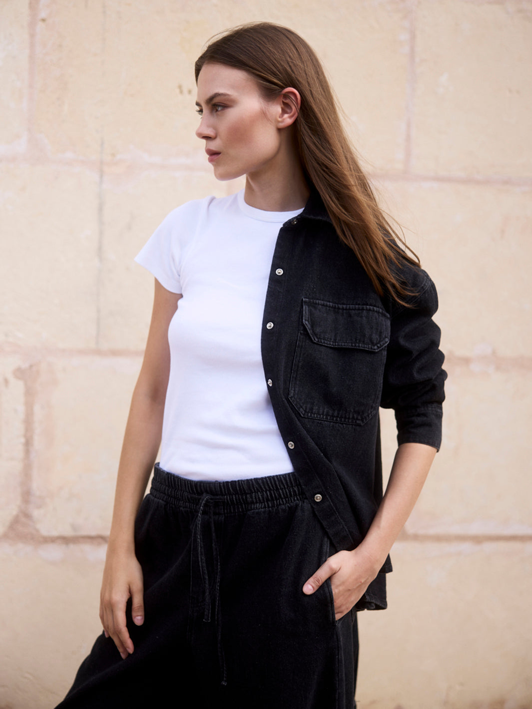 Damen Black Denim Overshirt aus Bio-Baumwolle im Porträt, halb geöffnet getragen über einem weißen T-Shirt.