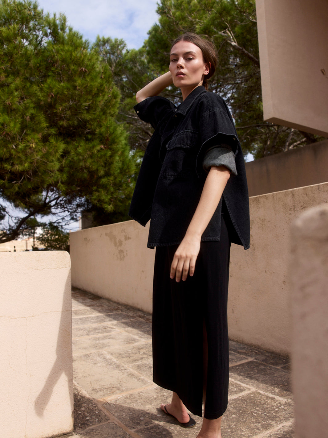 Damen Black Denim Overshirt aus Bio-Baumwolle in der seitlichen Ansicht, offen und mit gerollten Ärmeln über einem schwarzen Kleid.