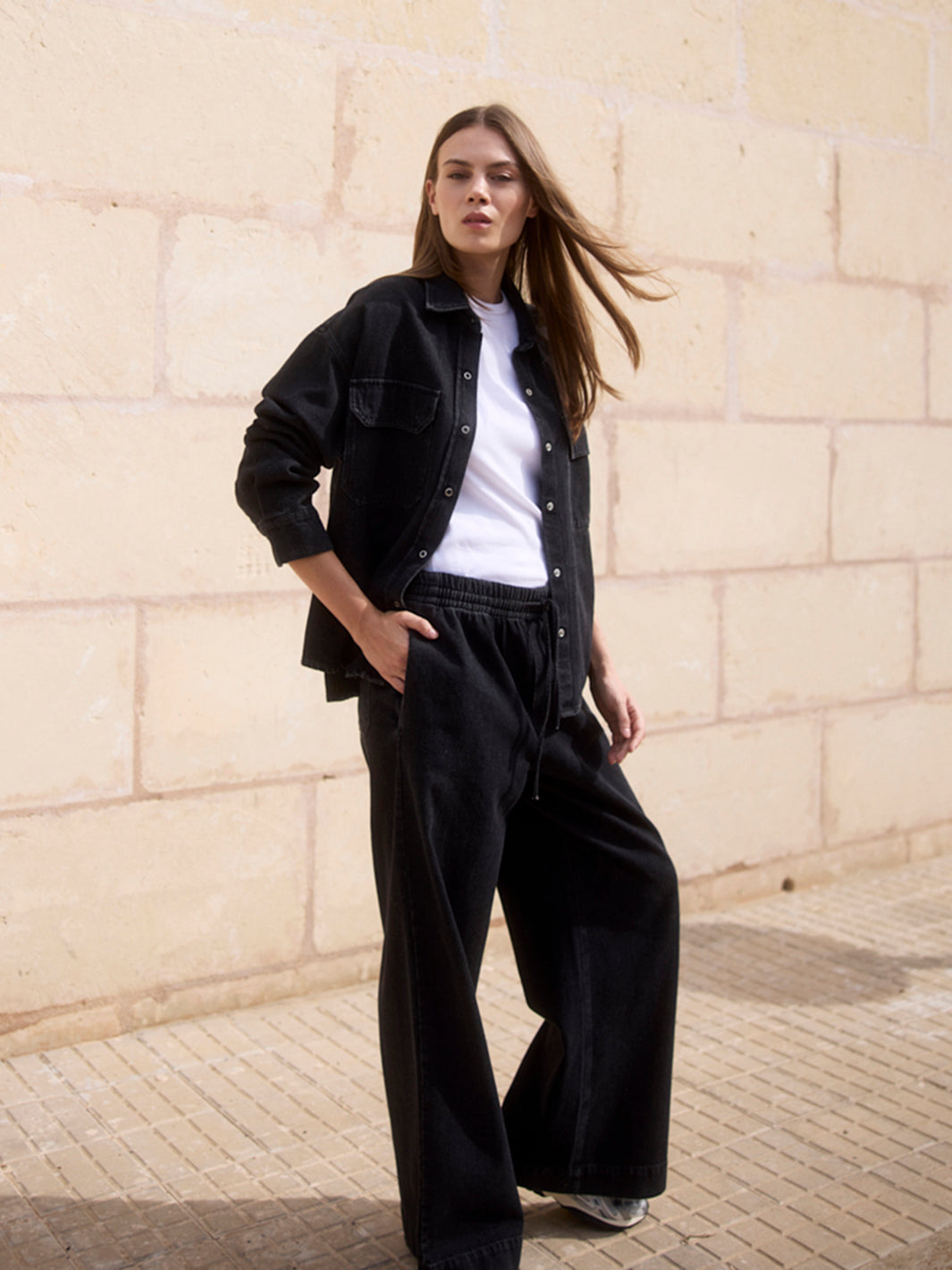 Damen Black Denim Overshirt aus Bio-Baumwolle in seitlicher Frontansicht, kombiniert mit weißem T-Shirt und Wide Leg Hose.
