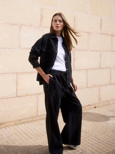 Damen Black Denim Overshirt aus Bio-Baumwolle in seitlicher Frontansicht, kombiniert mit weißem T-Shirt und Wide Leg Hose.