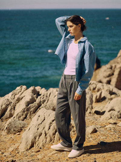 Frau trägt eine graue Classic Hose aus zertifizierter Wolle am Felsenstrand, locker geschnitten und mit Bundfalten.