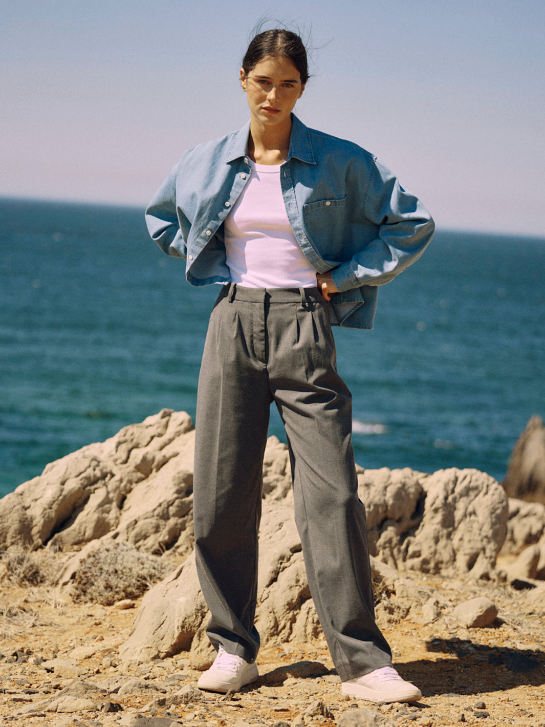 Frau trägt eine graue Classic Hose aus zertifizierter Wolle vor Felsen und Meer, mit Bundfalten und weitem Schnitt.