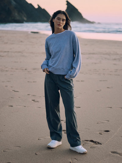 Frau trägt eine graue Classic Hose aus zertifizierter Wolle und einen hellgrauen Sweater am Strand in der Dämmerung.