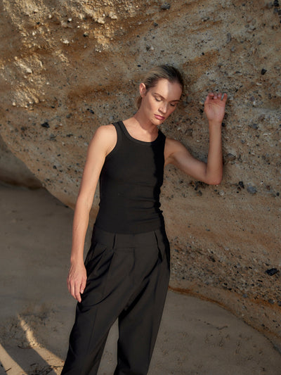 Frau trägt eine schwarze Classic Hose aus zertifizierter Wolle und ein schwarzes Top, angelehnt an eine sonnige Felswand.