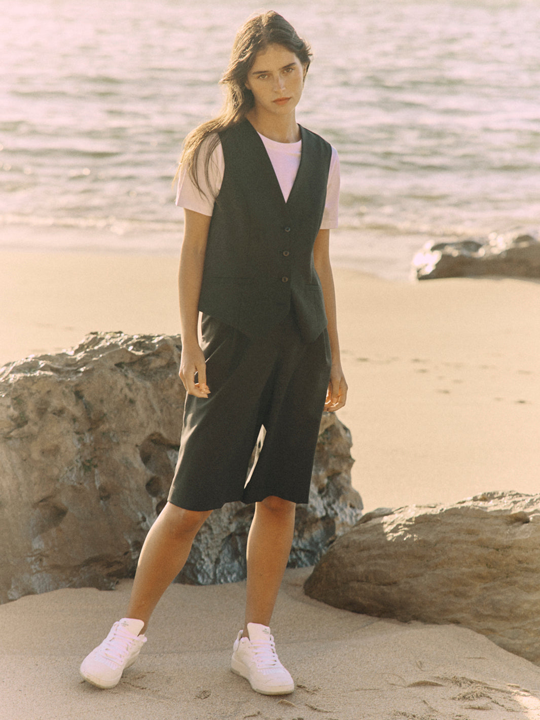 Modell trägt eine schwarze Bermuda aus zertifizierter Wolle im frontalen Look am Strand.