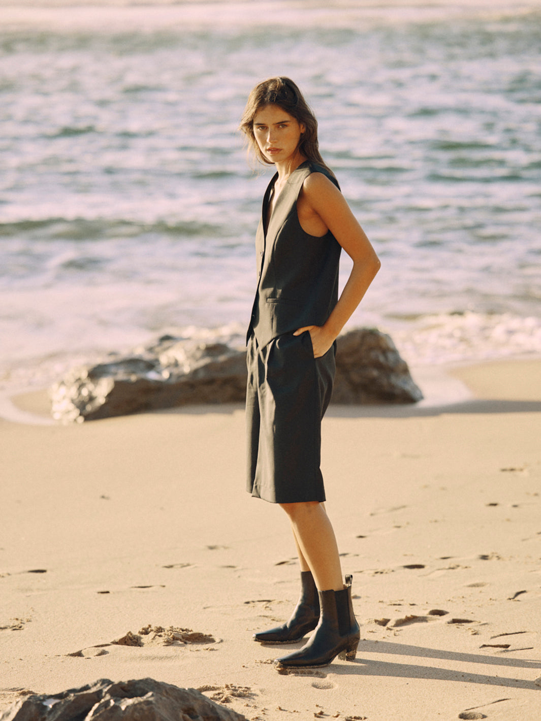 Modell trägt eine schwarze Bermuda aus zertifizierter Wolle in seitlicher Ansicht am Strand.