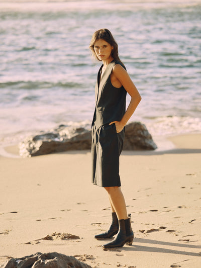 Modell trägt eine schwarze Bermuda aus zertifizierter Wolle in seitlicher Ansicht am Strand.