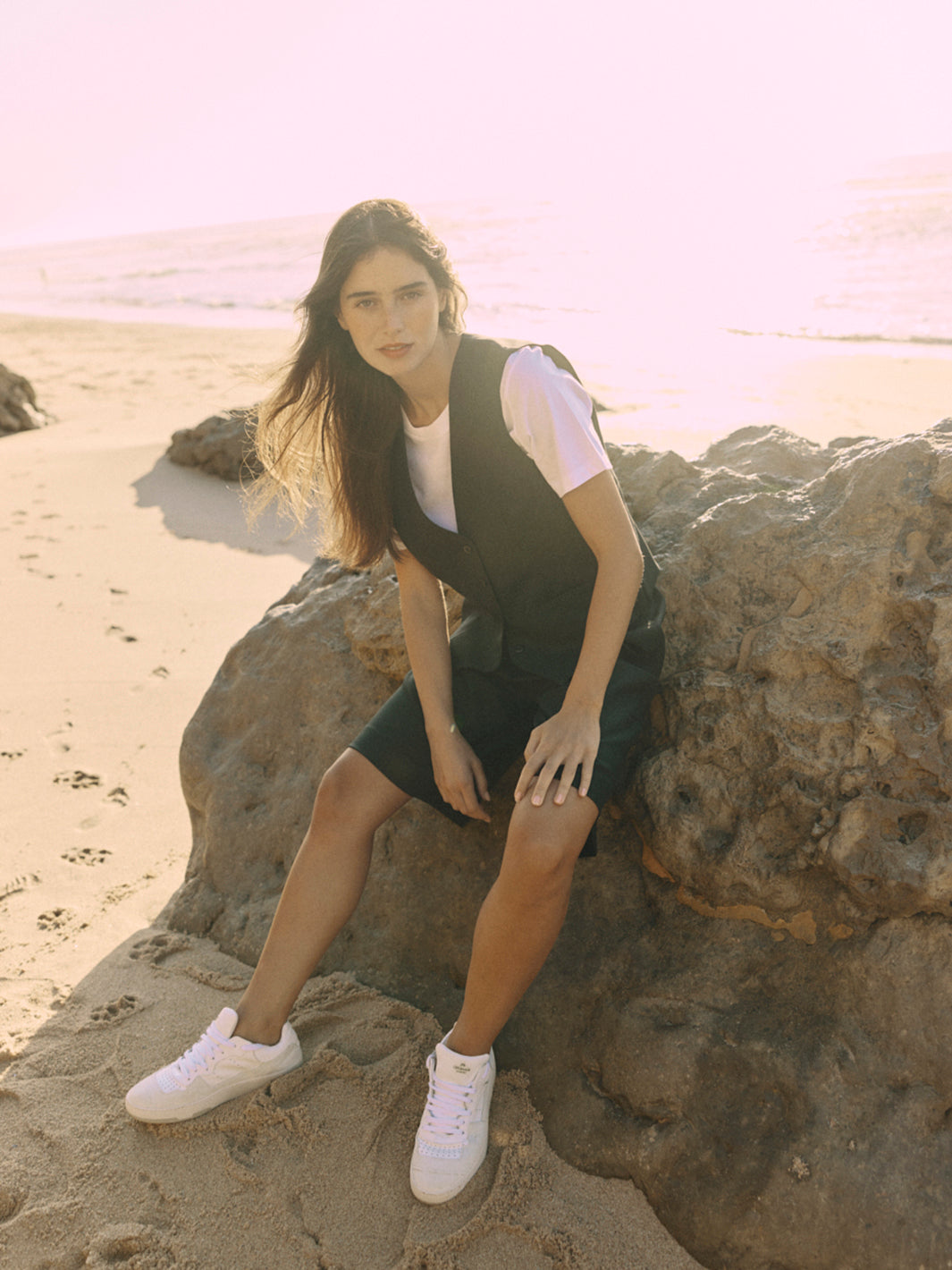 Modell trägt eine schwarze Bermuda aus zertifizierter Wolle, sitzend auf einem Felsen am Strand.