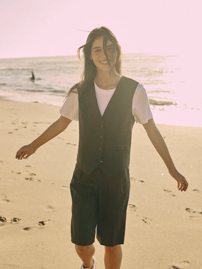 Modell trägt eine schwarze Bermuda aus zertifizierter Wolle, gehend am sonnigen Strand.