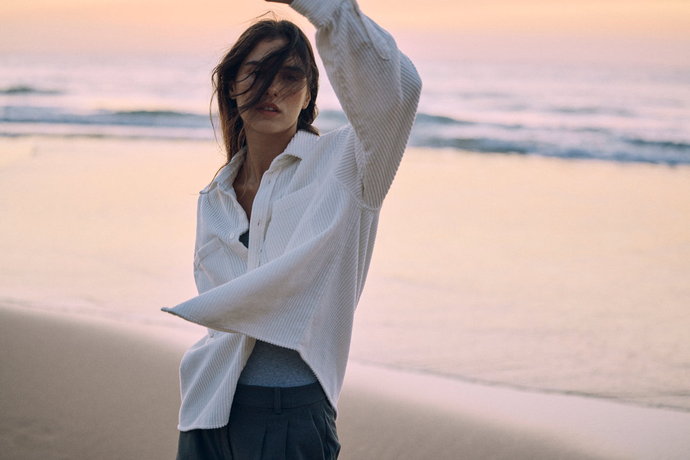 Modell trägt ein weißes Cord Overshirt aus Organic Cotton am Strand – minimalistisches Damen Editorial im Querformat.