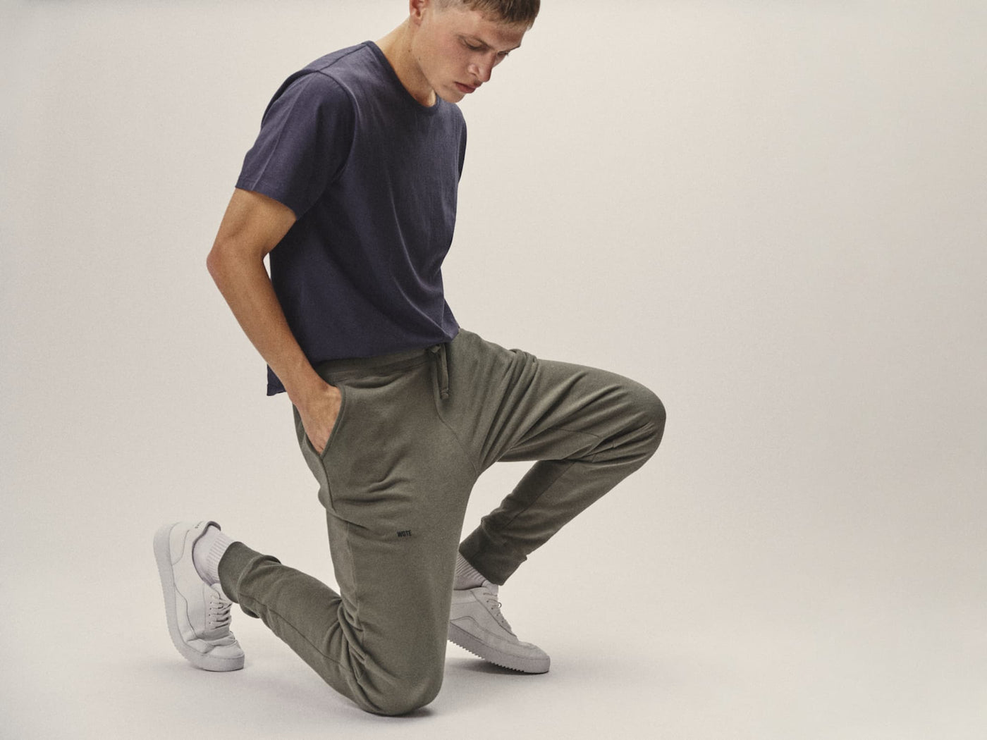 Model trägt olivgrüne WOTE Herren-Sweatpants aus Bio-Baumwolle in einer cleanen, modernen Studioaufnahme.