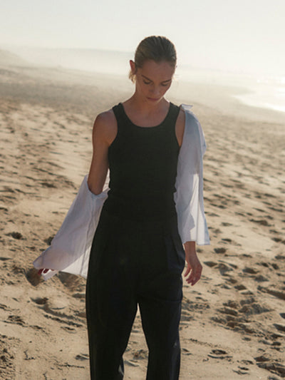 Geripptes Damen Tank Top in Schwarz mit höherem Rundhalsausschnitt aus Bio-Baumwolle mit Elasthan, clean und minimalistisch von WOTE - made in Portugal, Anschnitt Aufnahme mit Model am Strand mit Weißer Bluse über Schulter
