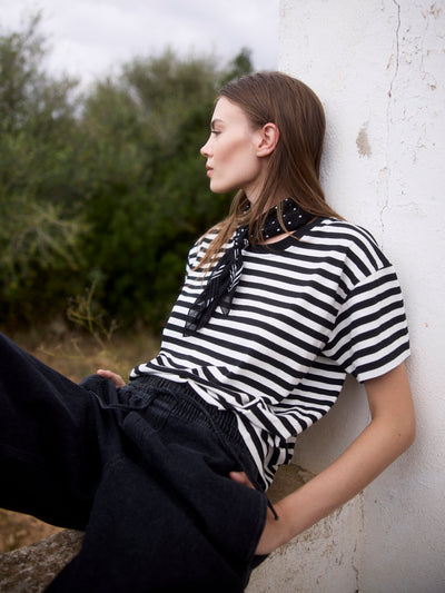 Modell trägt ein schwarz-weiß gestreiftes Relaxed-Fit T-Shirt aus Bio-Baumwolle, seitlich angelehnt.