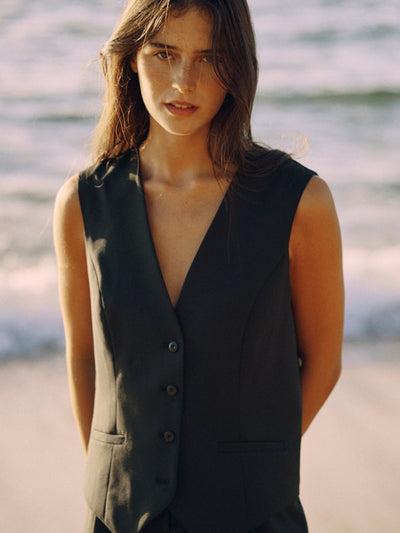 Modell trägt eine schwarze Weste aus nachhaltiger Tuchwolle in halbnaher Ansicht am Strand.