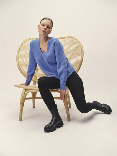 Damen Strick Pullover in Mittel-Blau mit V-Ausschnitt aus nachhaltiger Merino Wolle von WOTE - hergestellt in Italien, Frontansicht, Model sitzend