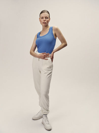 Frauen Tank Top gerippt in Blau aus 96% Bio-Baumwolle mit 4% Elasthan mit leicht tieferem Ausschnitt und figurbetontem Schnitt von WOTE - made in Portugal, Frontansicht Model im Studio mit Sweatpants in Off-White