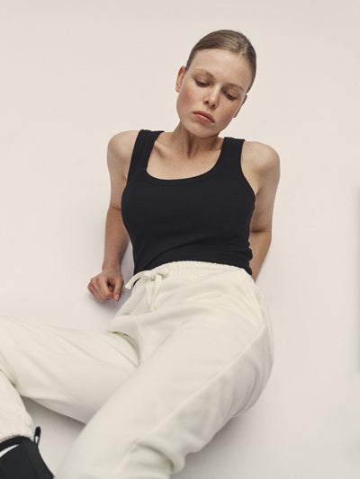 Damen Tank Top in Schwarz aus 96% Bio-Baumwolle mit 4% Elasthan, körpernaher Schnitt und tiefer Rundhalsausschnitt, nachhaltig in Portugal produziert - WOTE Classic Fit, Model im Studio mit Sweatpants in Off-White liegend
