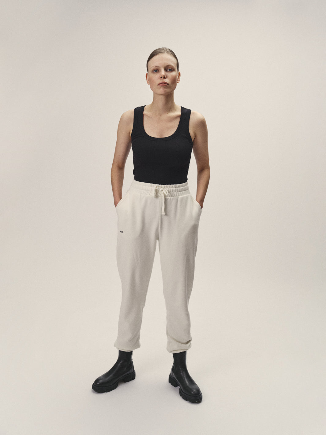 Rippen Tank Top in Schwarz für Damen aus 96% Bio-Baumwolle mit 4% Elasthan, enge Passform und tiefen Rundhalsausschnitt von WOTE, made in Portugal - Model im Studio stehend mit Sweatpants in Off-White