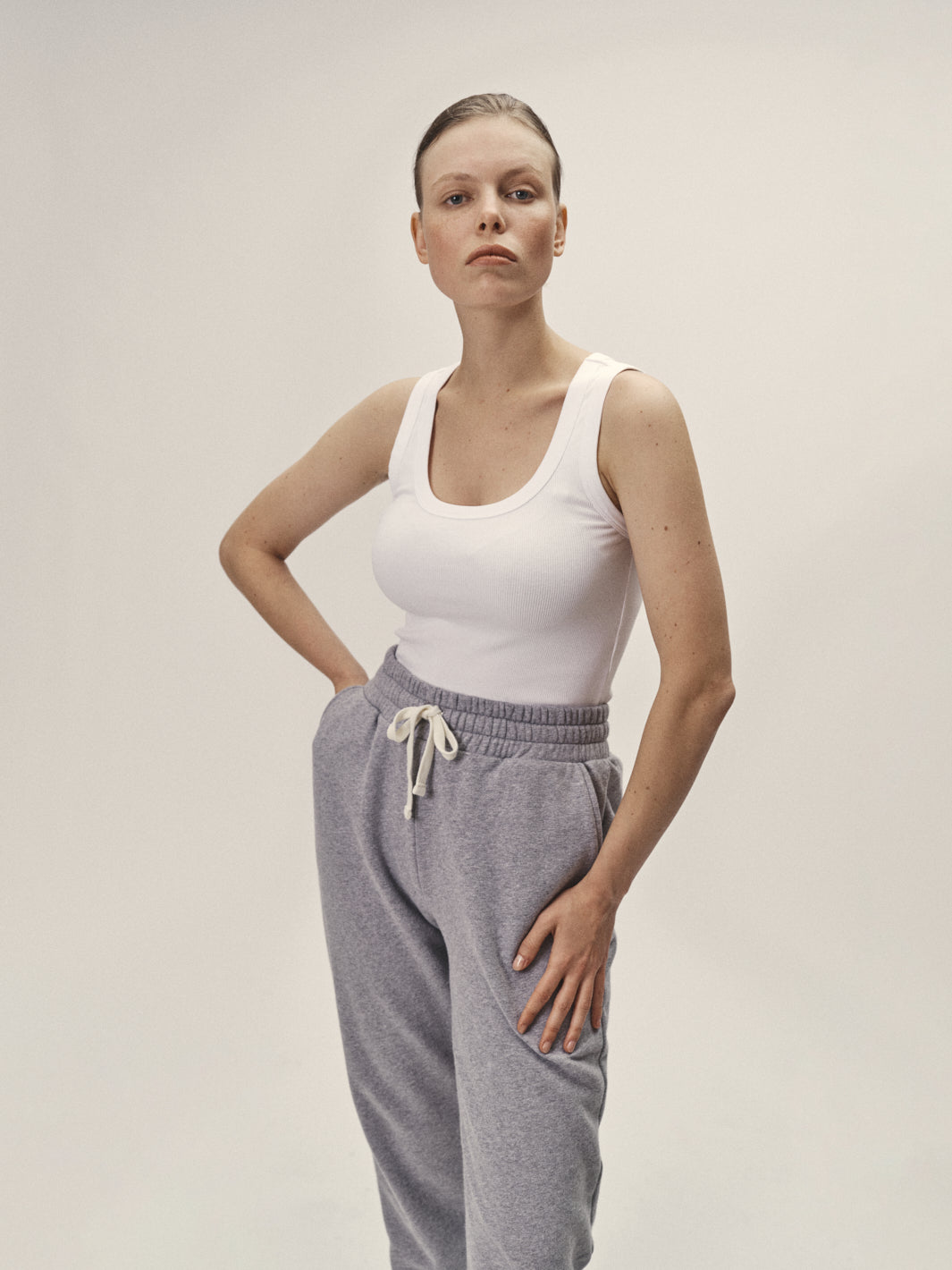Geripptes Damen Tank Top mit tiefen Rundhalsausschnitt in Weiß aus 96% Bio-Baumwolle und 4% Elasthan, fair und nachhaltig in Portugal produziert von WOTE - Frontansicht mit Model im Studio mit Sweathose in Grau-Melange